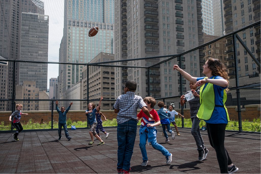 a photograph of kids and a chaperone playing football on a rooftop in downtown chicago. the photo was taken by CPS lives artist Moe Zoyari at Ogden International